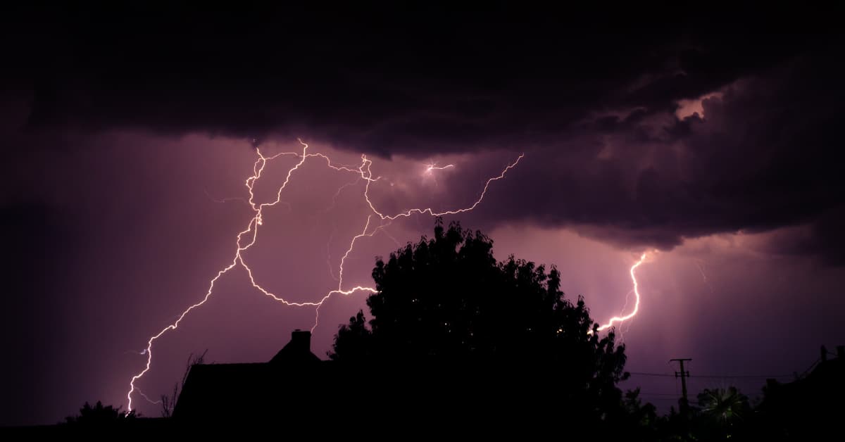 A dramatic nighttime landscape showcases intense lightning illuminating a dark sky.